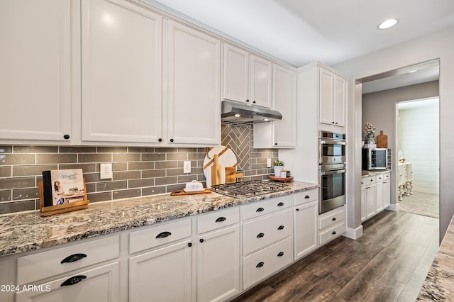 kitchen featuring under cabinet range hood, dark wood finished floors, decorative backsplash, stainless steel appliances, and white cabinetry