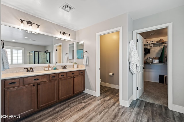 full bathroom featuring wood finished floors, visible vents, double vanity, a sink, and a shower stall