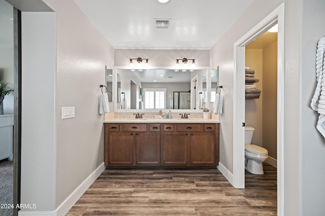 full bath with visible vents, toilet, double vanity, wood finished floors, and a sink