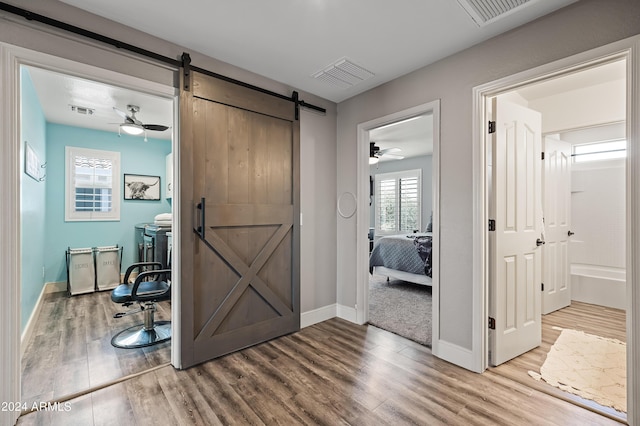 hall with a barn door, wood finished floors, and visible vents