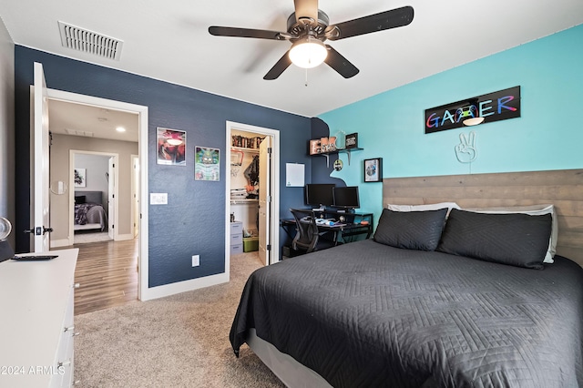 carpeted bedroom featuring a walk in closet, baseboards, visible vents, and a ceiling fan