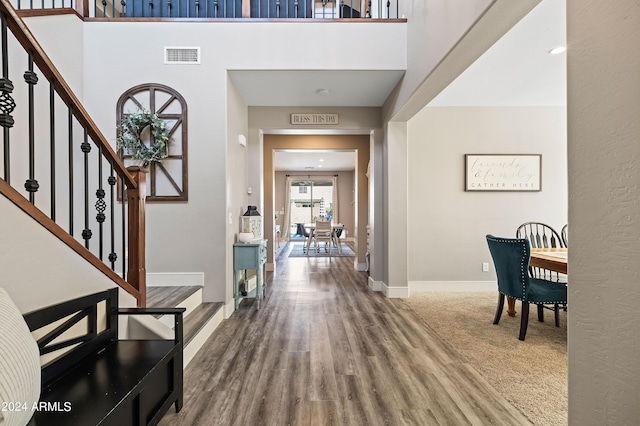 entrance foyer featuring visible vents, wood finished floors, baseboards, a towering ceiling, and stairs