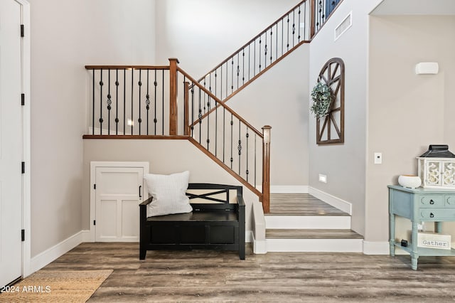 staircase featuring visible vents, a high ceiling, baseboards, and wood finished floors