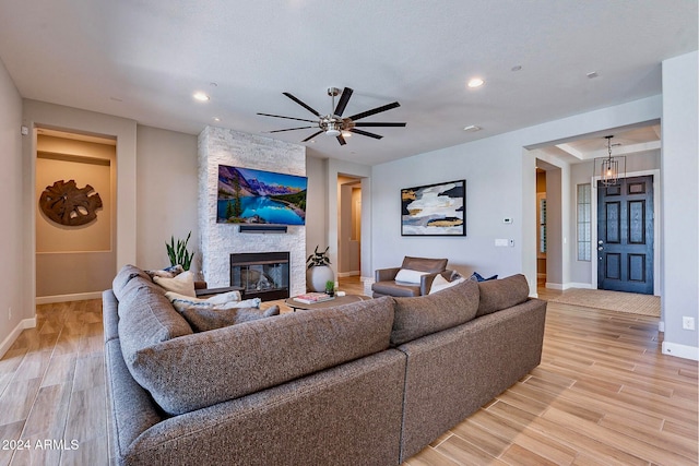 living room featuring ceiling fan, light hardwood / wood-style floors, and a stone fireplace