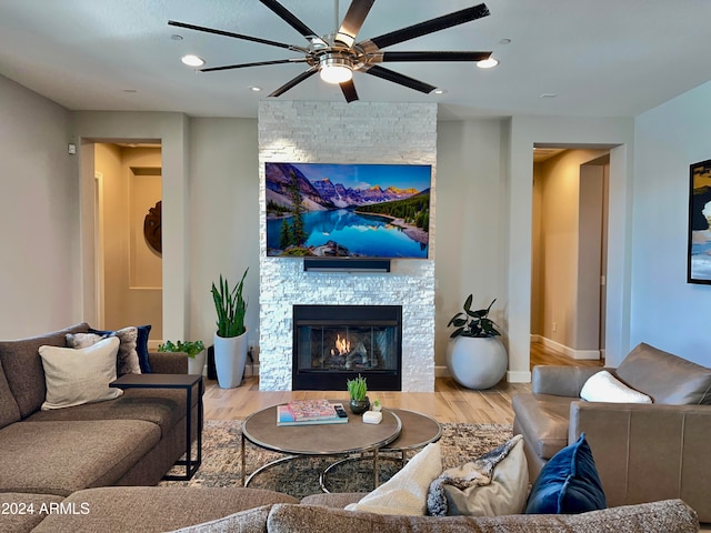 living room with ceiling fan, a stone fireplace, and wood-type flooring