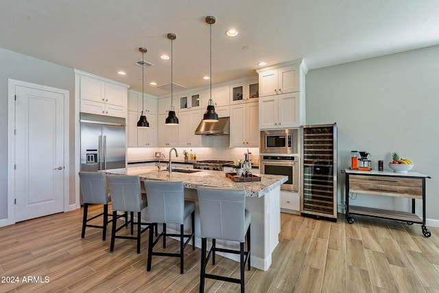 kitchen with built in appliances, white cabinetry, sink, range hood, and light wood-type flooring