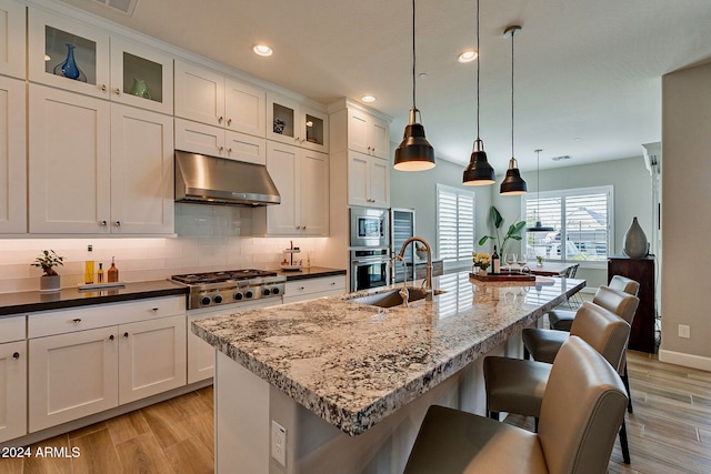 kitchen featuring appliances with stainless steel finishes, decorative light fixtures, a kitchen bar, light hardwood / wood-style floors, and a kitchen island with sink