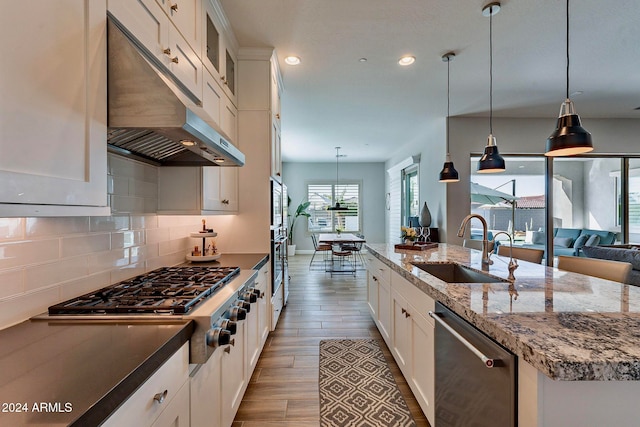 kitchen featuring stainless steel appliances, white cabinetry, sink, hanging light fixtures, and light wood-type flooring