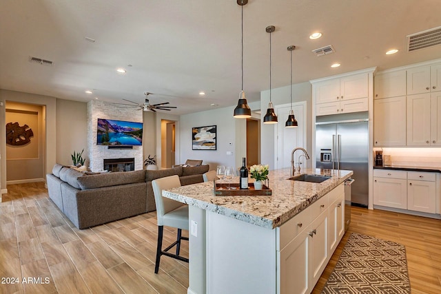 kitchen with stainless steel built in fridge, light stone counters, sink, an island with sink, and white cabinetry