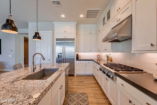 kitchen featuring stainless steel appliances, white cabinetry, light wood-type flooring, decorative light fixtures, and sink