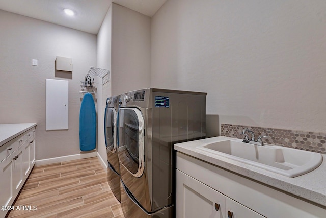 laundry room with washing machine and dryer, cabinets, sink, and light hardwood / wood-style flooring