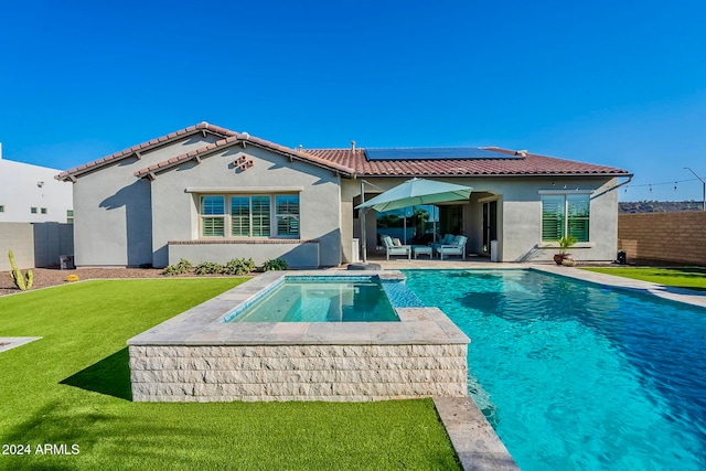 back of property with a yard, solar panels, a patio, and a pool with hot tub