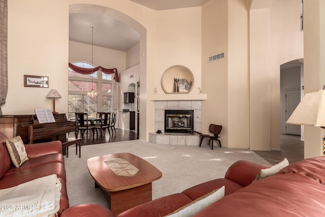 living area with visible vents, a tile fireplace, a towering ceiling, carpet floors, and a chandelier