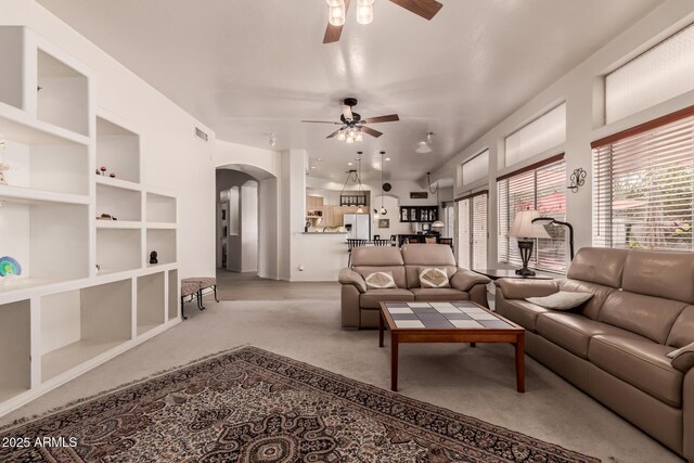 carpeted living room featuring a ceiling fan, arched walkways, and built in shelves
