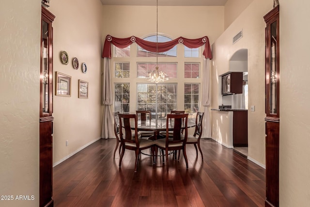 dining space featuring baseboards, visible vents, dark wood-type flooring, a high ceiling, and a notable chandelier