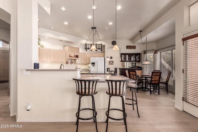 kitchen featuring decorative light fixtures, light wood finished floors, tasteful backsplash, white fridge with ice dispenser, and a peninsula