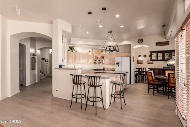 kitchen featuring white refrigerator with ice dispenser, dark countertops, decorative light fixtures, a peninsula, and a kitchen bar