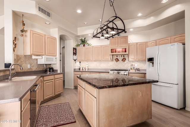 kitchen with white appliances, a sink, a kitchen island, visible vents, and light brown cabinetry