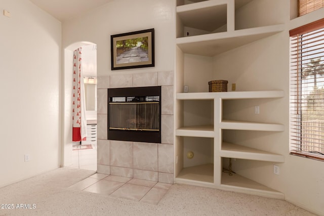 unfurnished living room featuring built in shelves, arched walkways, carpet flooring, and a fireplace