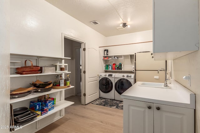 laundry area featuring washing machine and clothes dryer, visible vents, a sink, light wood-type flooring, and laundry area