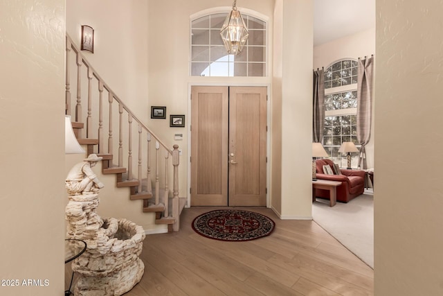 entrance foyer featuring stairs, an inviting chandelier, a towering ceiling, and light wood-style floors