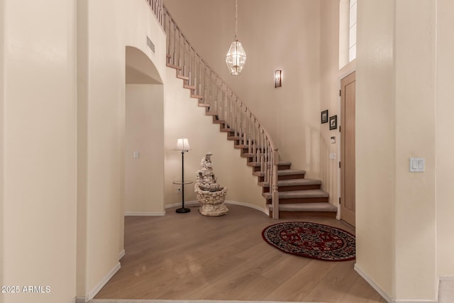 entrance foyer with visible vents, a towering ceiling, wood finished floors, baseboards, and stairs