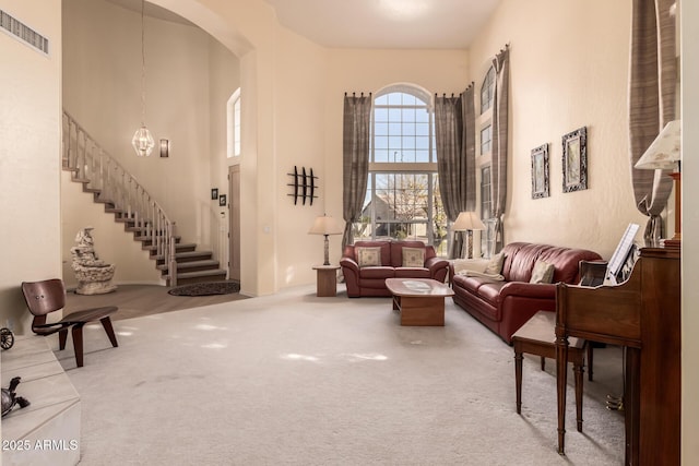living area with visible vents, arched walkways, a towering ceiling, stairway, and carpet flooring