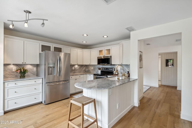 kitchen featuring appliances with stainless steel finishes, a sink, a peninsula, glass insert cabinets, and light wood-style flooring