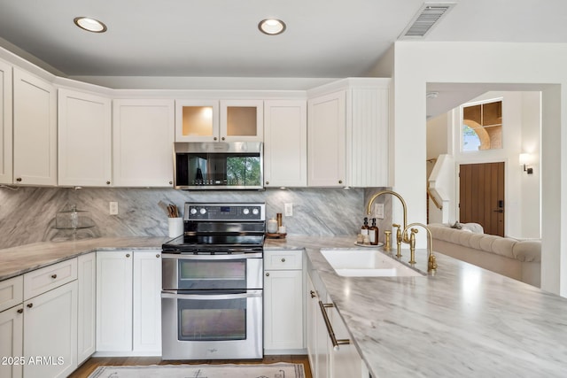 kitchen featuring appliances with stainless steel finishes, a sink, white cabinets, light stone counters, and backsplash