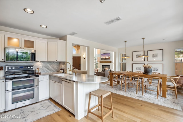 kitchen with appliances with stainless steel finishes, a sink, a peninsula, a glass covered fireplace, and light wood-style floors