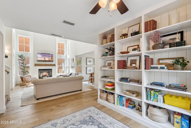 living area with a glass covered fireplace, wood finished floors, ceiling fan, and baseboards