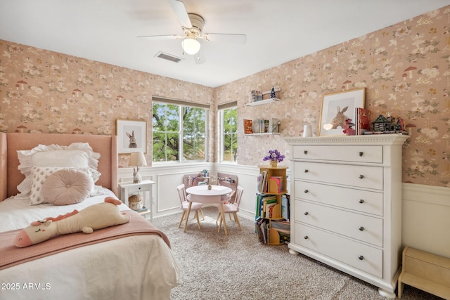 carpeted bedroom with wallpapered walls, a wainscoted wall, and a ceiling fan