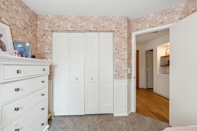 bedroom featuring wallpapered walls, a closet, a wainscoted wall, and wood finished floors