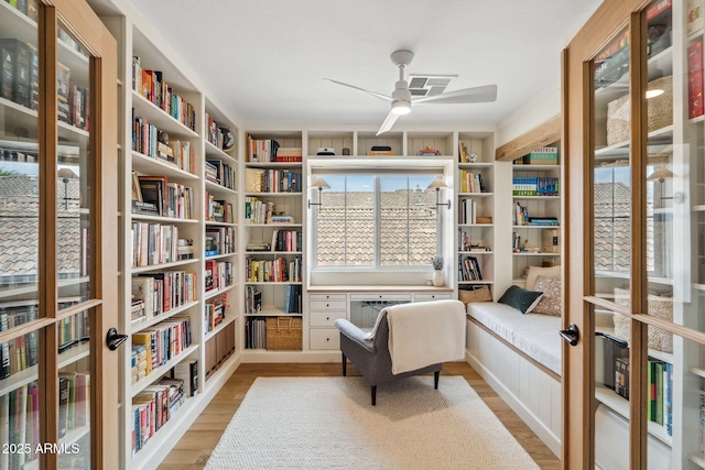 living area with wall of books, ceiling fan, and light wood-type flooring