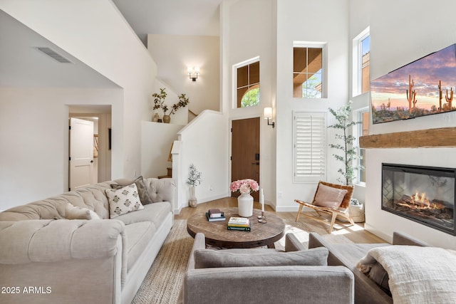 living room featuring a high ceiling, wood finished floors, stairway, a glass covered fireplace, and baseboards