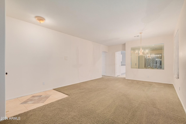 empty room featuring light carpet, a notable chandelier, arched walkways, and light tile patterned floors