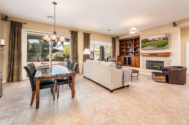 living room with a tile fireplace, ceiling fan with notable chandelier, and built in features