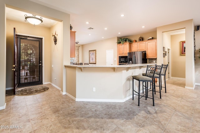 kitchen featuring black microwave, a kitchen breakfast bar, kitchen peninsula, stainless steel fridge, and light brown cabinetry