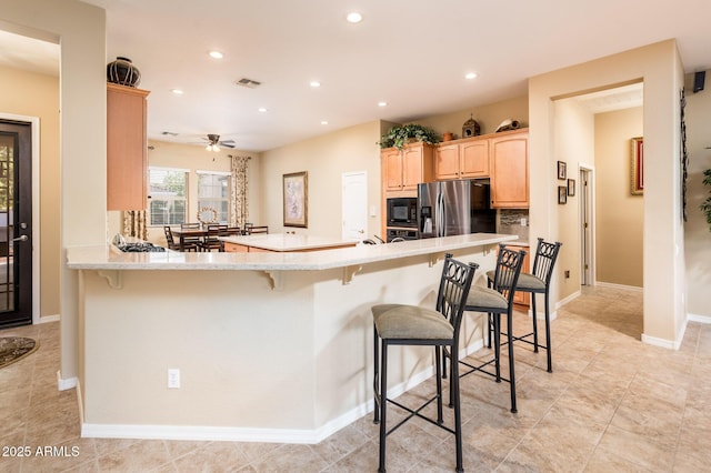 kitchen featuring black microwave, a kitchen breakfast bar, kitchen peninsula, stainless steel fridge, and light brown cabinetry