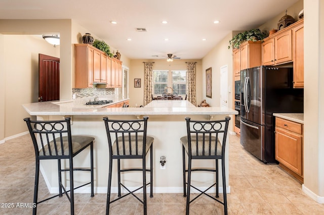 kitchen with kitchen peninsula, a kitchen breakfast bar, tasteful backsplash, ceiling fan, and fridge with ice dispenser