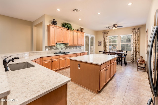 kitchen featuring ceiling fan, sink, light stone counters, a kitchen island, and appliances with stainless steel finishes