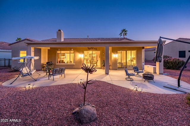 back house at dusk featuring a fire pit and a patio area