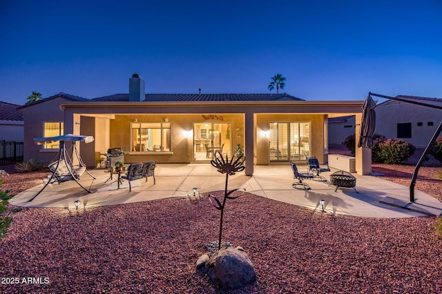 back house at dusk featuring a fire pit and a patio