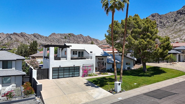 contemporary house with a balcony, an attached garage, a mountain view, a front lawn, and driveway