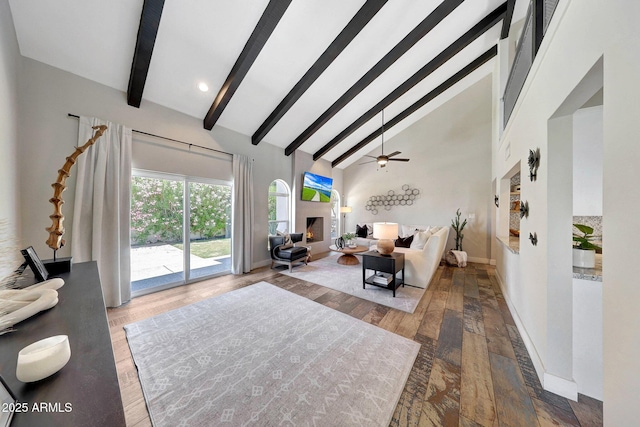 living room with beamed ceiling, ceiling fan, hardwood / wood-style floors, a warm lit fireplace, and high vaulted ceiling