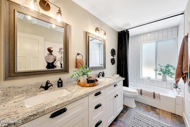 full bath featuring toilet, shower / bath combo with shower curtain, double vanity, and stone tile flooring