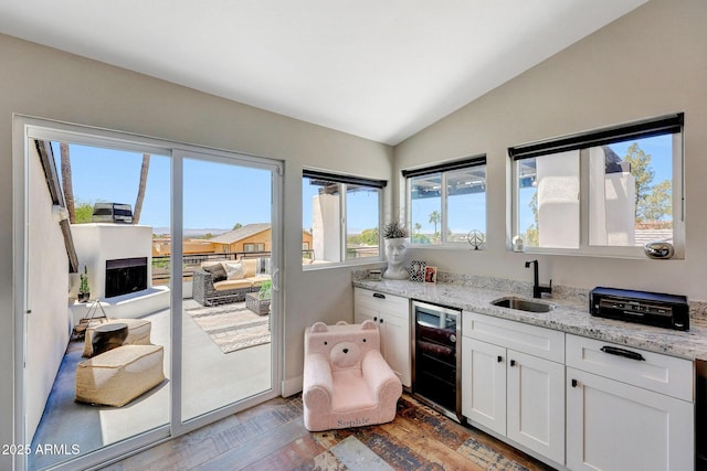 kitchen featuring a sink, wine cooler, vaulted ceiling, white cabinetry, and light stone countertops