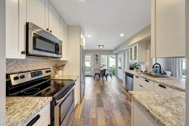 kitchen with appliances with stainless steel finishes, a sink, hardwood / wood-style flooring, white cabinets, and recessed lighting