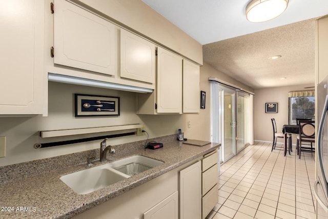 kitchen with light tile patterned floors, a textured ceiling, white cabinetry, light stone counters, and a sink