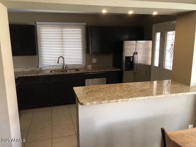 kitchen featuring a sink, appliances with stainless steel finishes, a peninsula, light tile patterned flooring, and dark cabinets